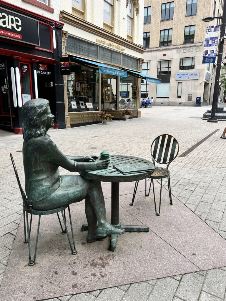 metal statue of woman sitting at table with 2 chairs