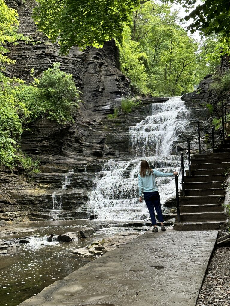 Female holding onto stair rail leaning off path looking at waterfall flowing into gorge